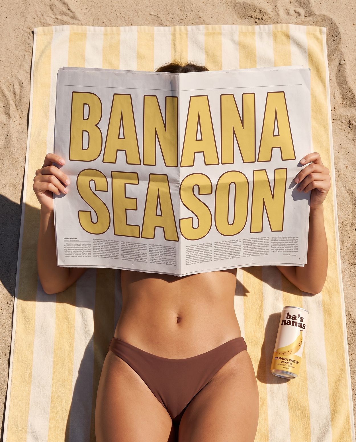 Sunbather on a striped towel reading a Banana Season newspaper, a can of Ba's Nanas beside her