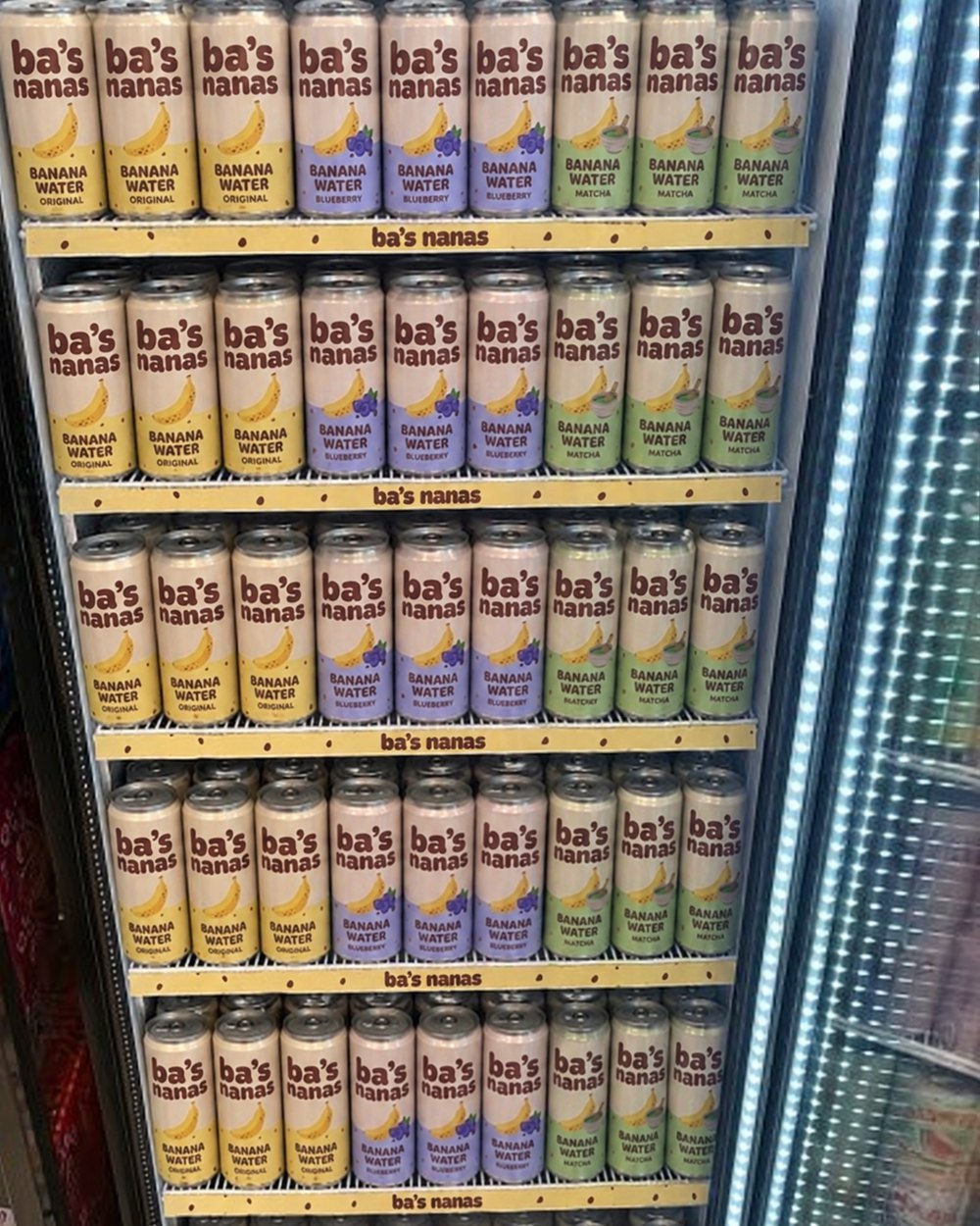 A glass-door cooler packed with Original, Blueberry and Matcha cans and freckled ba's nanas shelf strips
